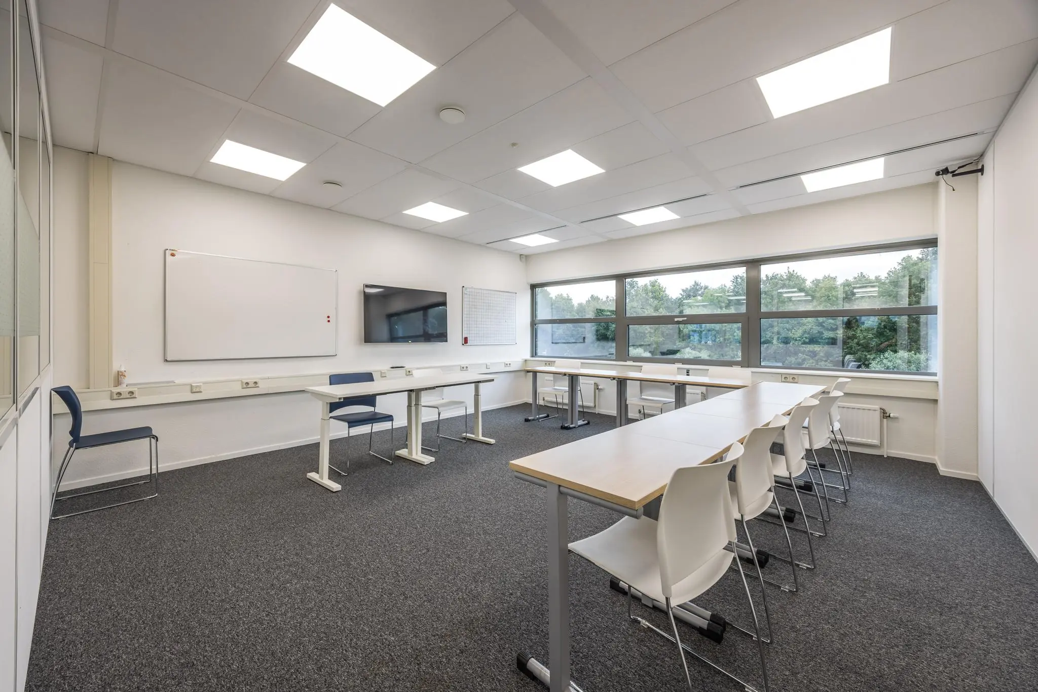 Moderne vergaderruimte aan de Daltonlaan met U-opstelling, whiteboards, scherm en grote ramen met uitzicht op groen.