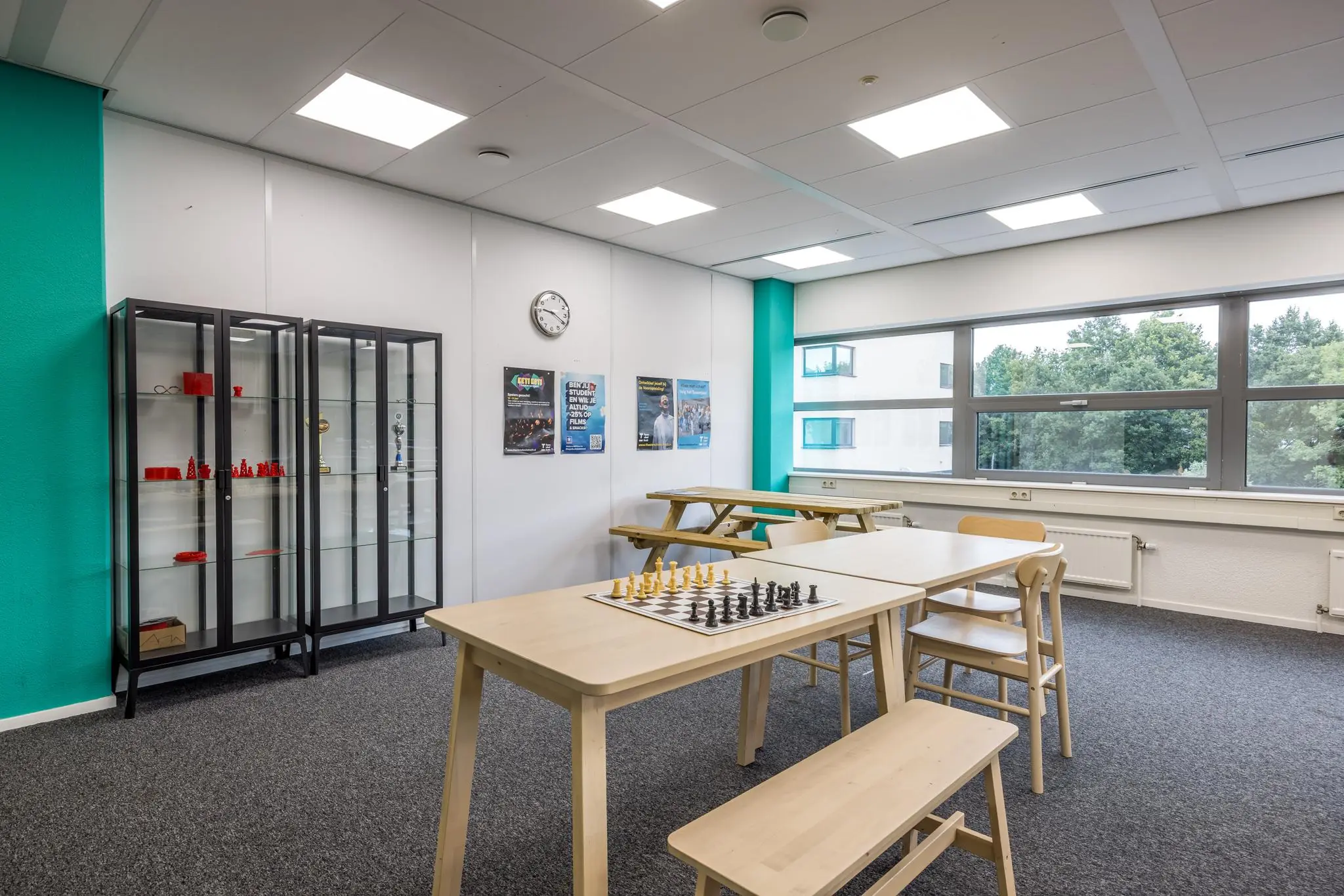 Kantineruimte op Daltonlaan met houten tafels, vitrinekasten en een schaakbord op tafel.