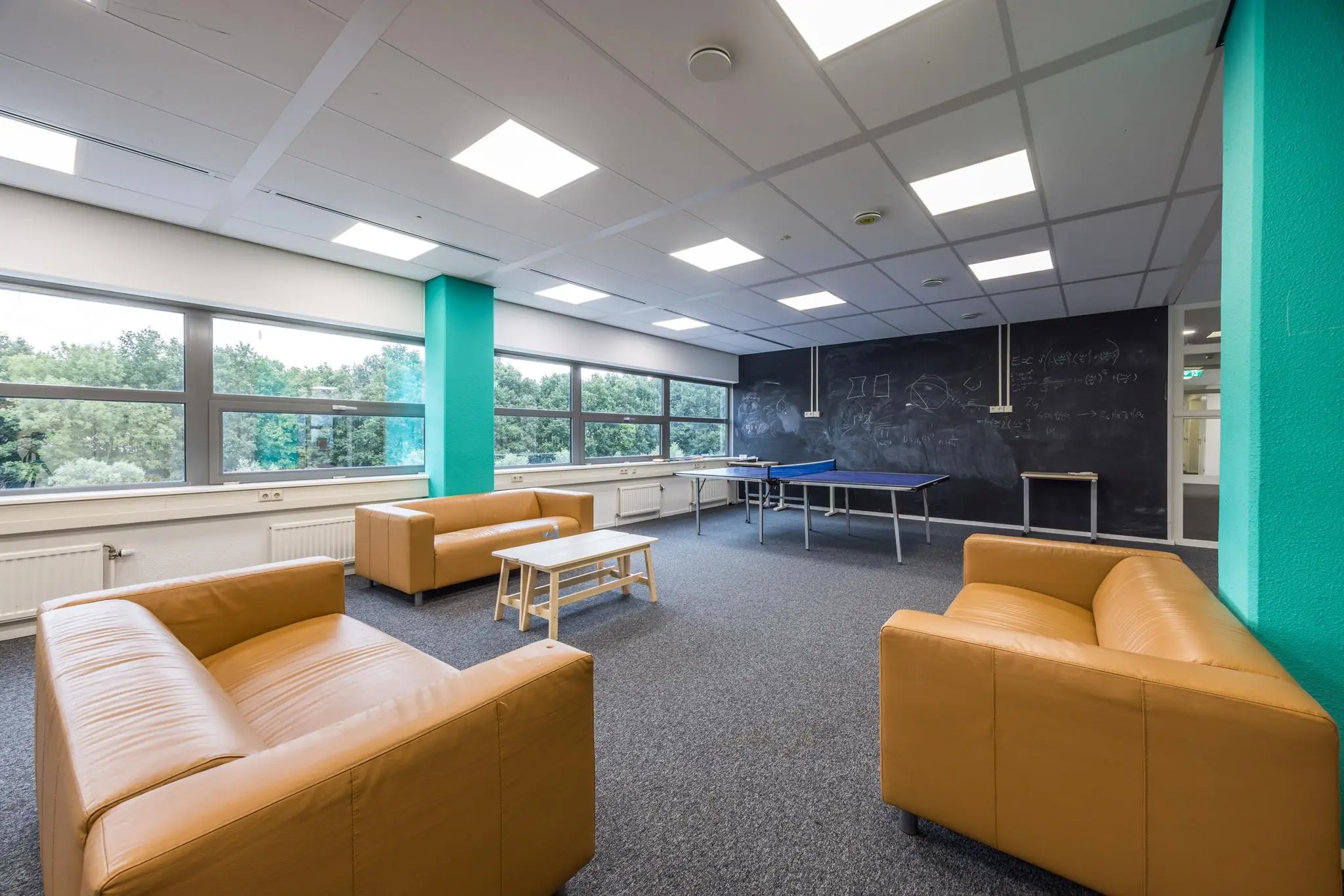 Moderne lounge- en recreatieruimte op Daltonlaan met zitbanken, tafeltennistafel en een schoolbordmuur.