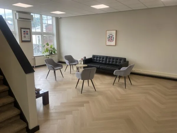 Moderne wachtruimte aan het Lange Voorhout met grijze stoelen, zwarte bank, houten visgraatvloer en grote ramen.