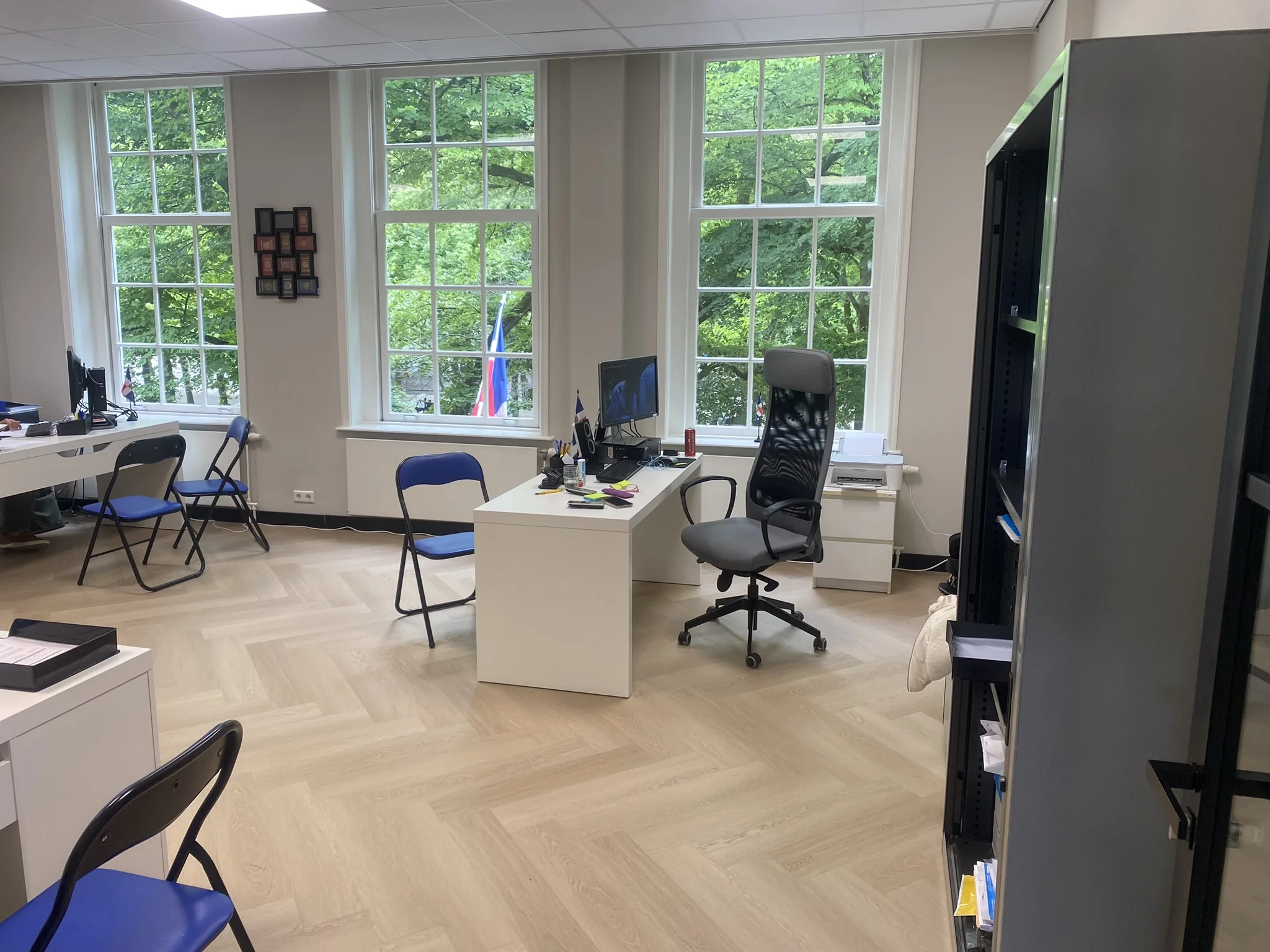 Modern kantoor met meerdere bureaus en stoelen, gelegen aan het Lange Voorhout met uitzicht op groene bomen buiten de grote ramen.