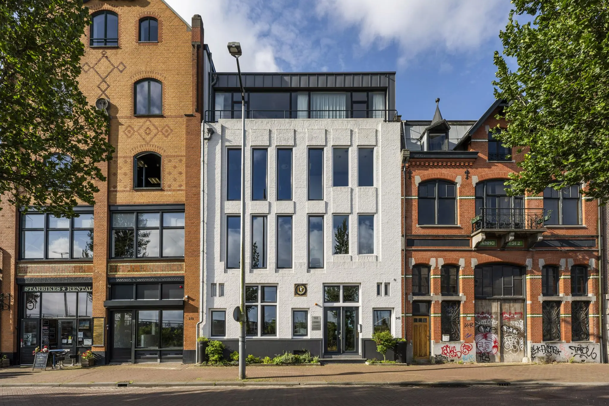 Voorgevel van drie karakteristieke panden aan de De Ruijterkade in Amsterdam, met diverse bouwstijlen en details.