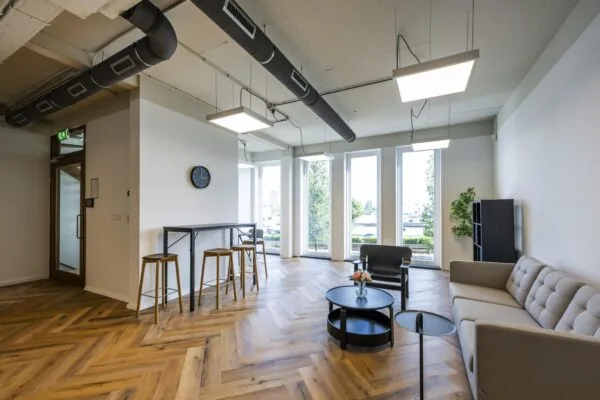 Moderne wachtruimte op De Ruijterkade met houten visgraatvloer, grote ramen, een zitgedeelte en hoge tafel met barkrukken.