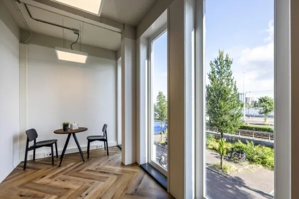 Lichte hoekruimte met twee stoelen en een tafel, uitkijkend op De Ruijterkade via grote ramen.