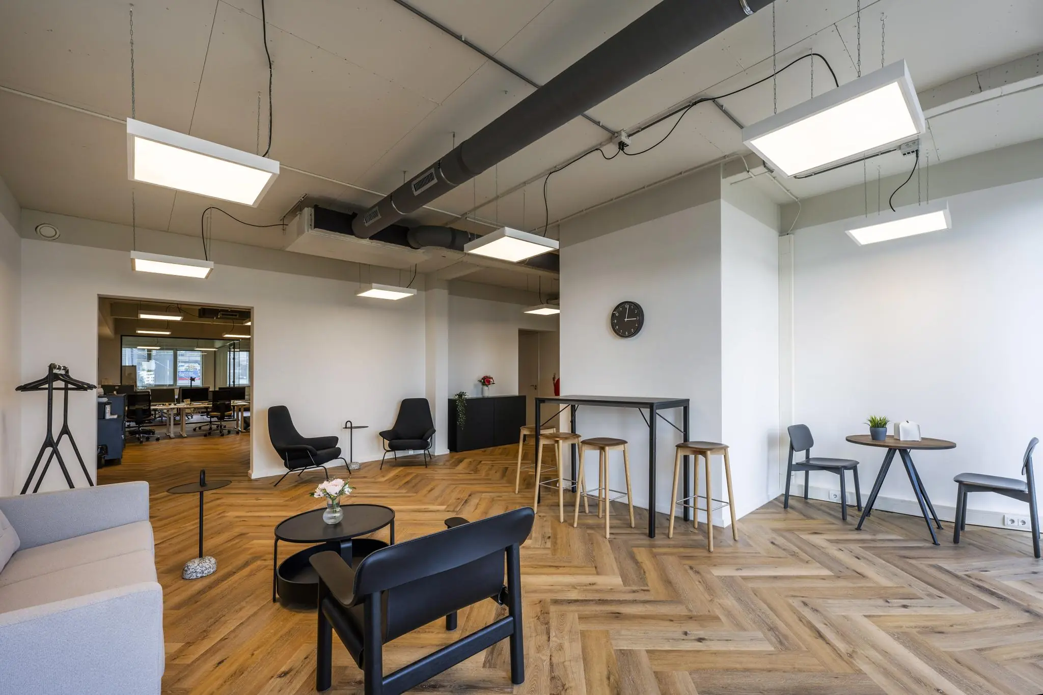 Moderne lounge- en werkruimte aan de De Ruijterkade met houten visgraatvloer, zitgelegenheden en industriële plafondverlichting.