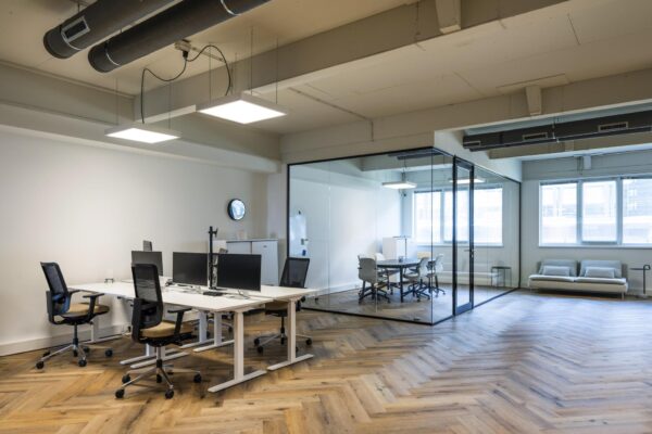 Modern kantoorinterieur aan de De Ruijterkade met werkplekken, een glazen vergaderruimte en een zithoek.