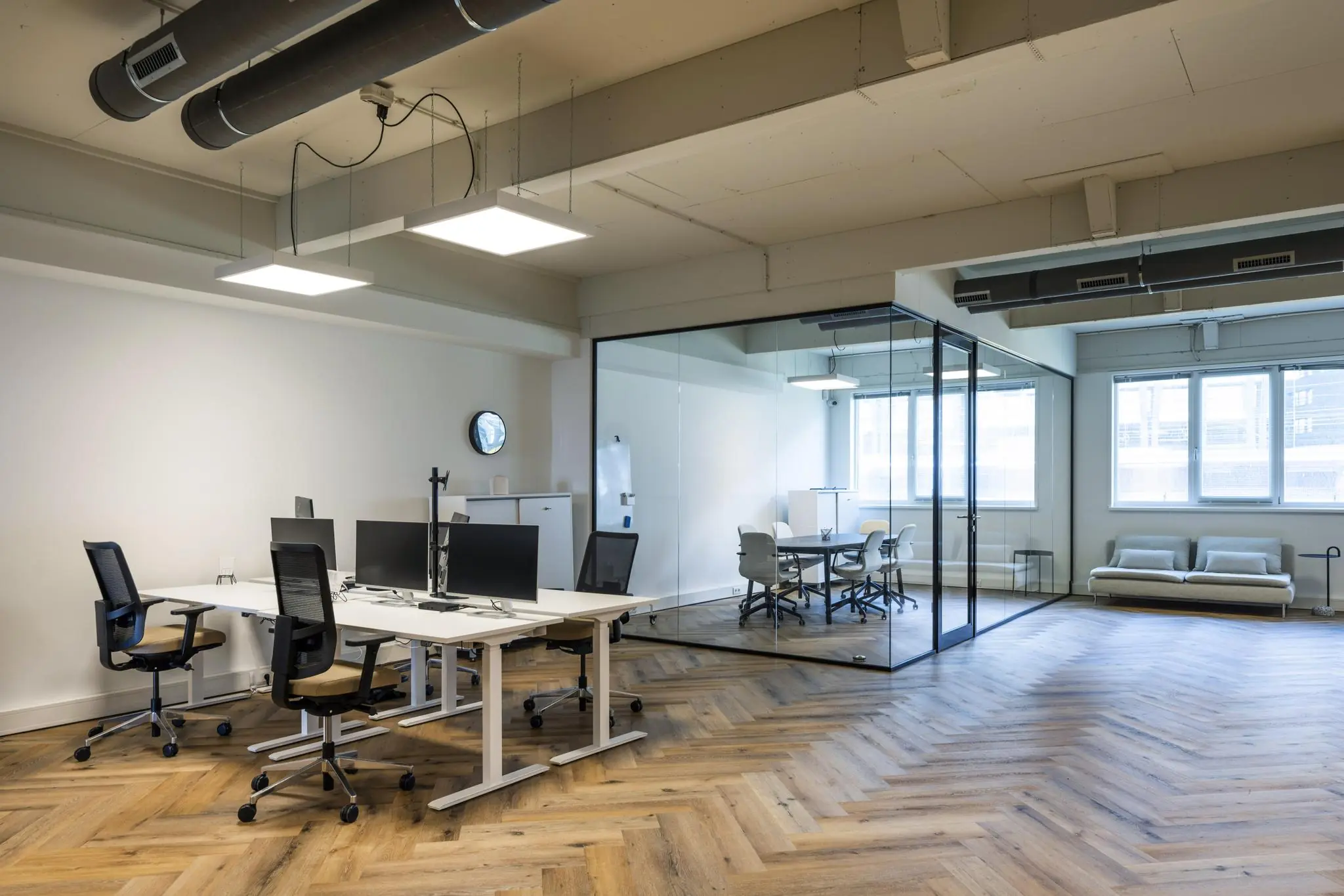 Modern kantoorinterieur aan de De Ruijterkade met werkplekken, een glazen vergaderruimte en een zithoek.