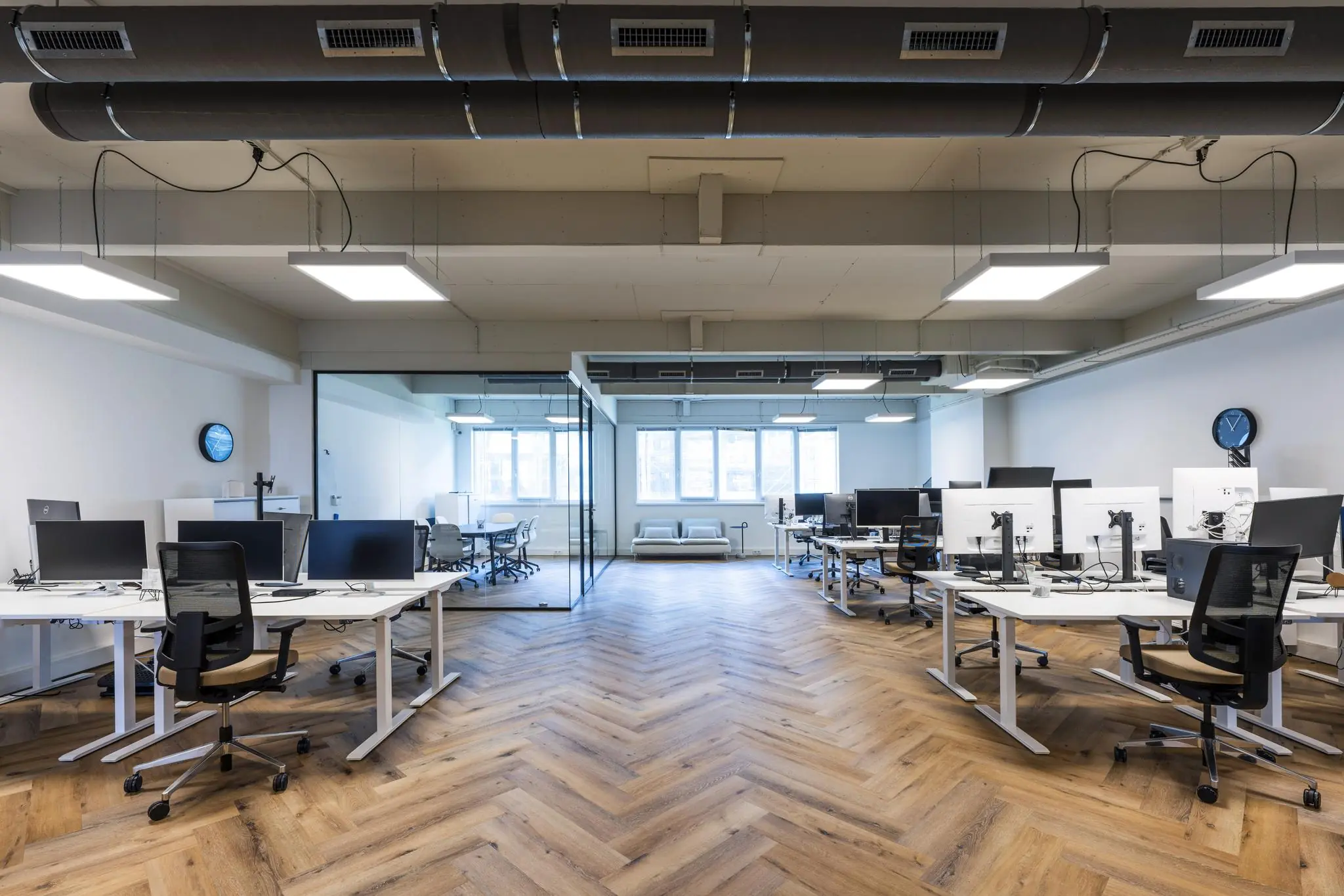 Modern kantoorinterieur aan de De Ruijterkade met open werkplekken, glazen vergaderruimte en visgraat houten vloer.