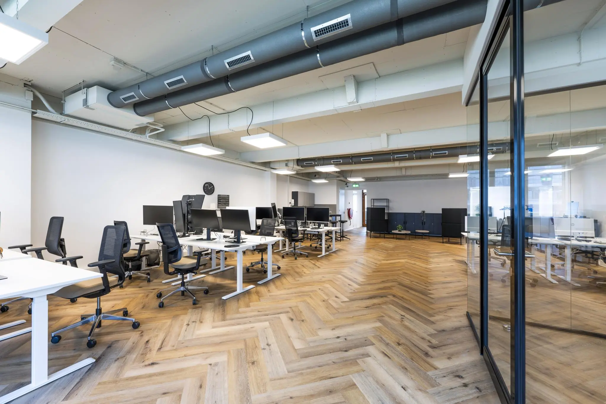 Modern kantoorinterieur aan de De Ruijterkade met open werkplekken, houten visgraatvloer en glazen vergaderruimte.