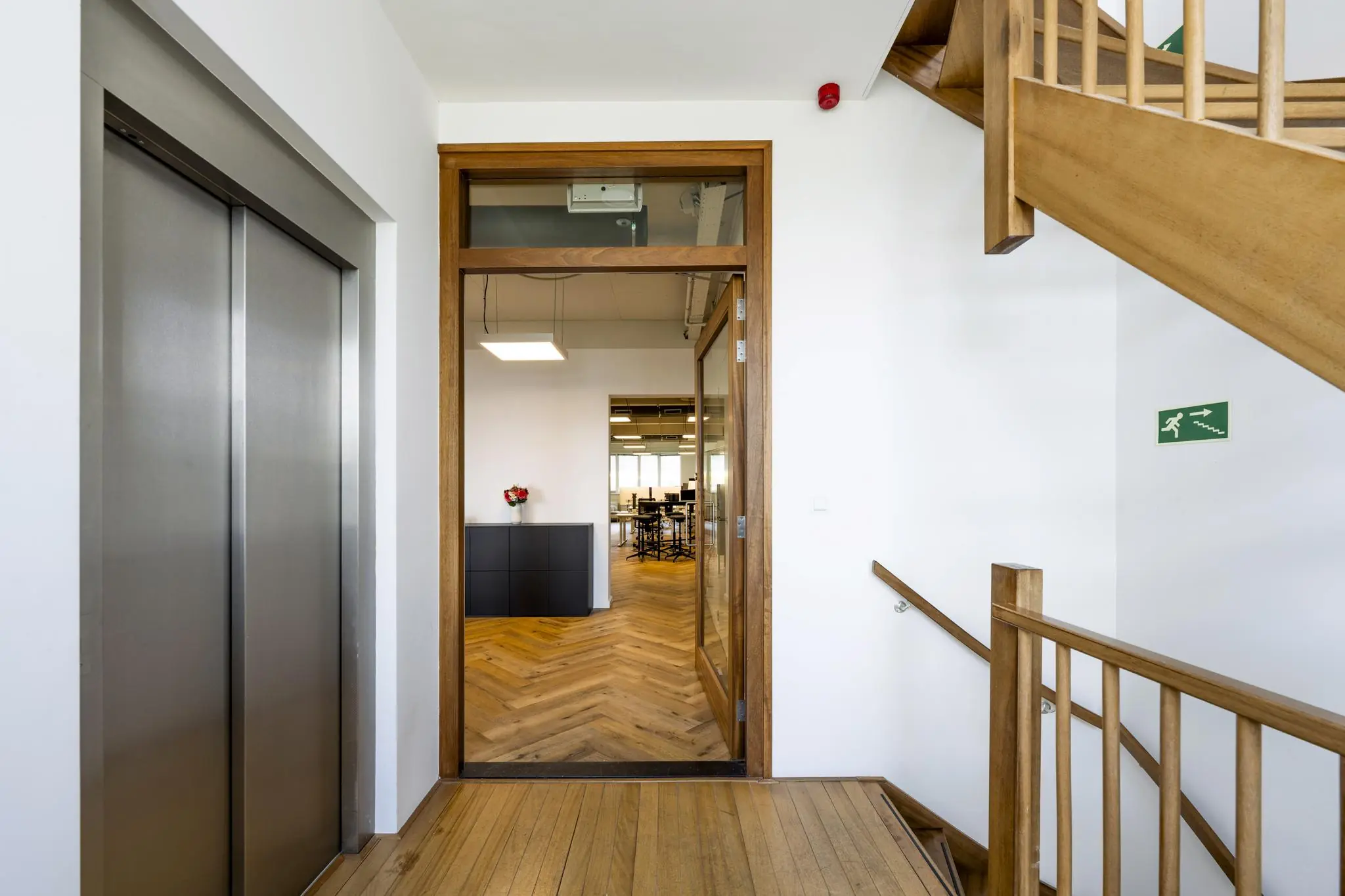 Ingang van een modern kantoor aan de De Ruijterkade, met houten trap, lift en glazen deur naar een vergaderruimte.