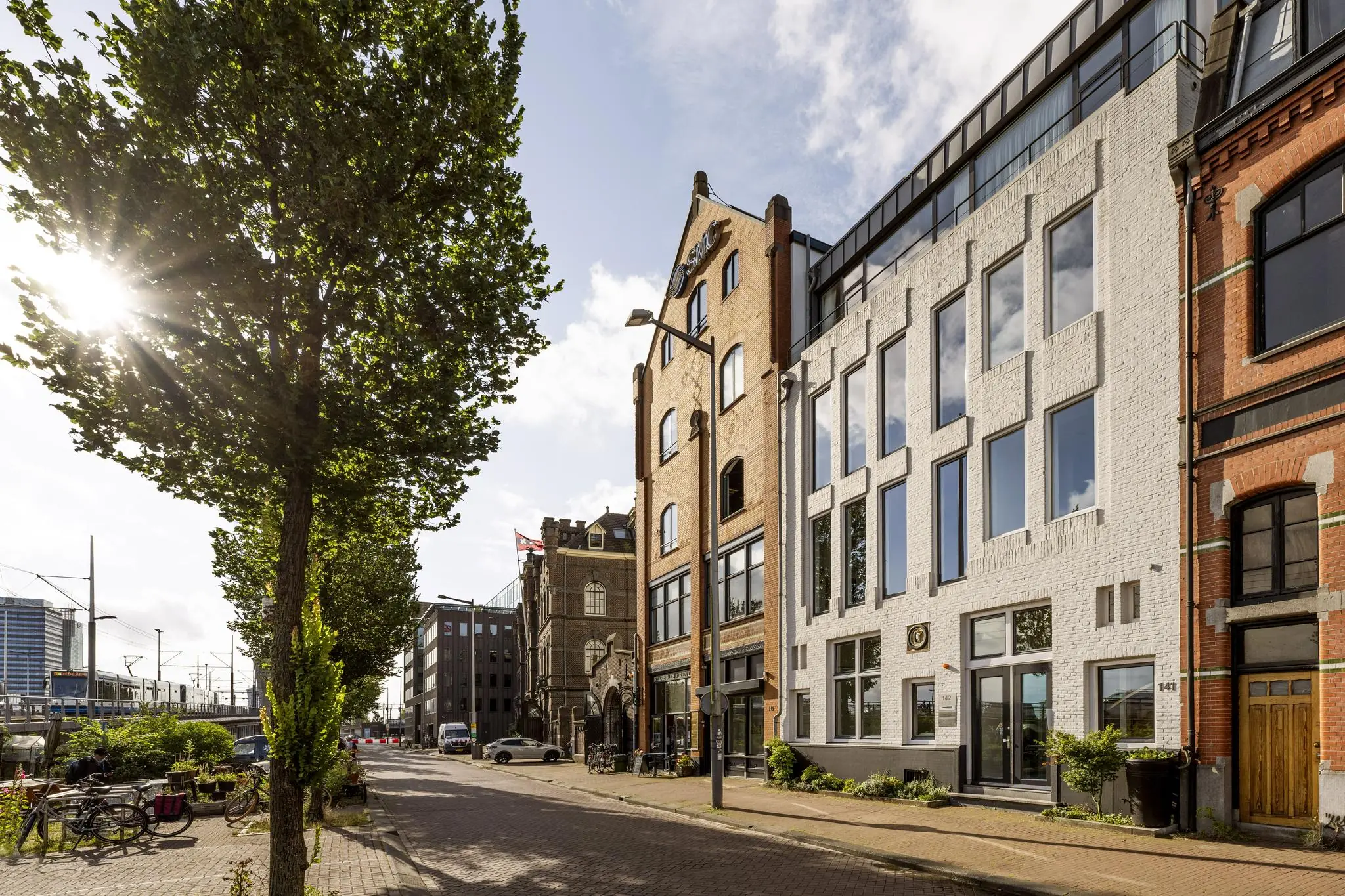 Zonnige straat aan de De Ruijterkade in Amsterdam met historische gevels en moderne panden.