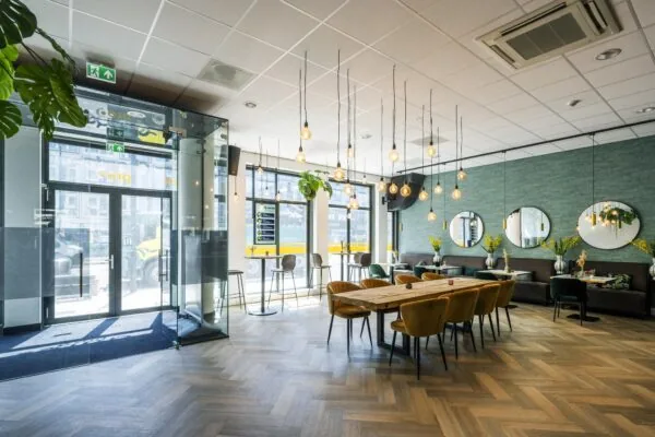 Modern en licht restaurantinterieur aan het Elizabeth Cady Stantonplein met houten vloer, lange eettafel en sfeerverlichting.