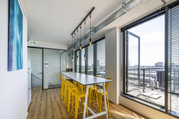 Moderne vergaderruimte met lange tafel, gele barkrukken en uitzicht op het Elizabeth Cady Stantonplein via een open glazen deur.