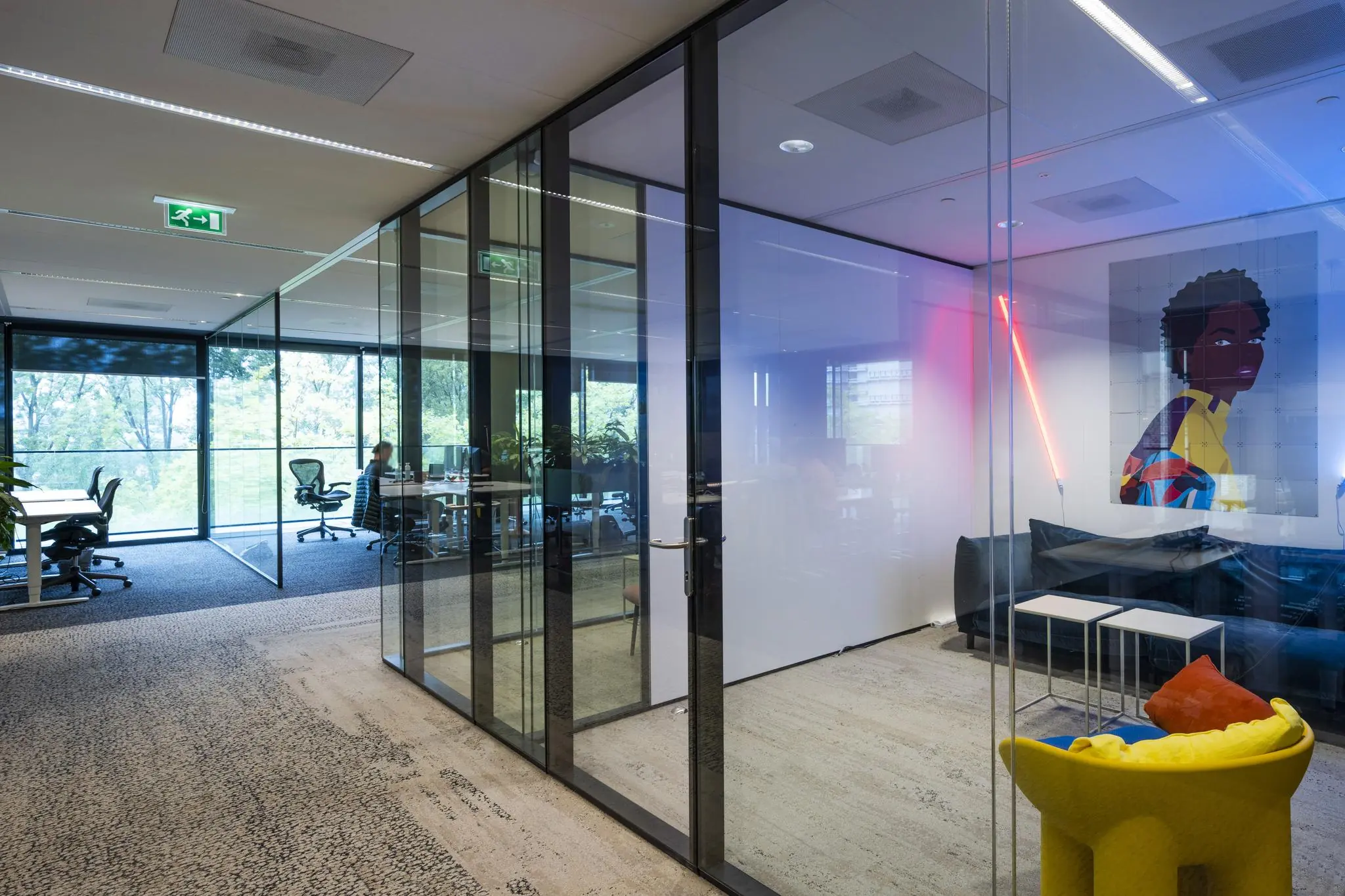 Modern kantoorinterieur aan de Gustav Mahlerlaan met glazen vergaderruimtes, kleurrijke kunst en zitmeubilair.