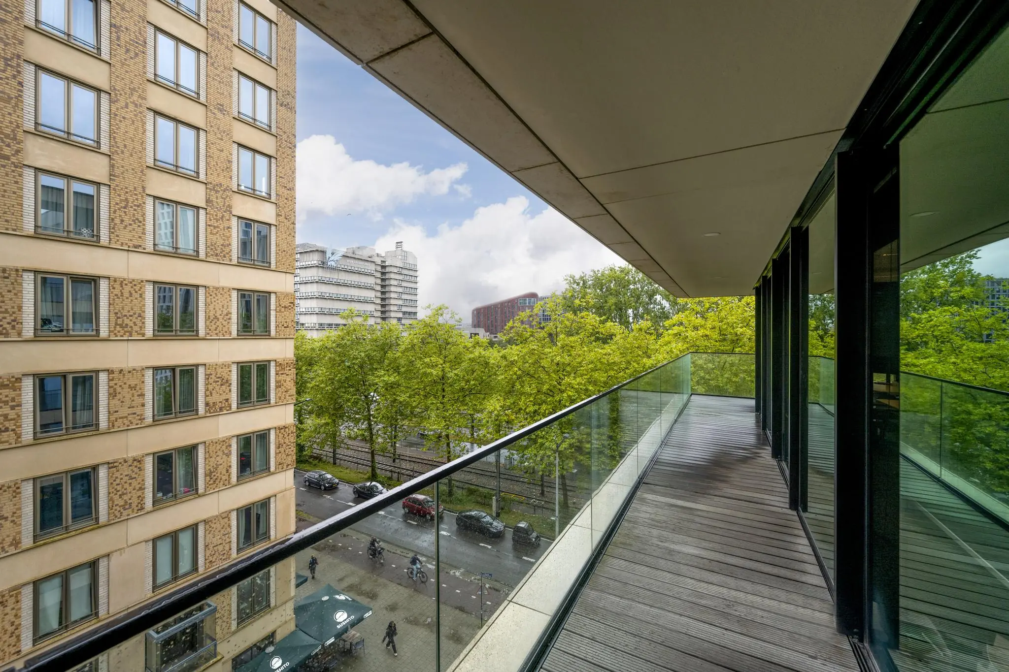 Modern balkon met glazen balustrade aan de Gustav Mahlerlaan, met uitzicht op een groene laan en omliggende kantoorpanden.