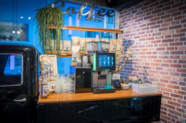 Koffiehoek met een zelfbedieningskoffiemachine, koffiebenodigdheden en decoratie tegen een bakstenen muur.