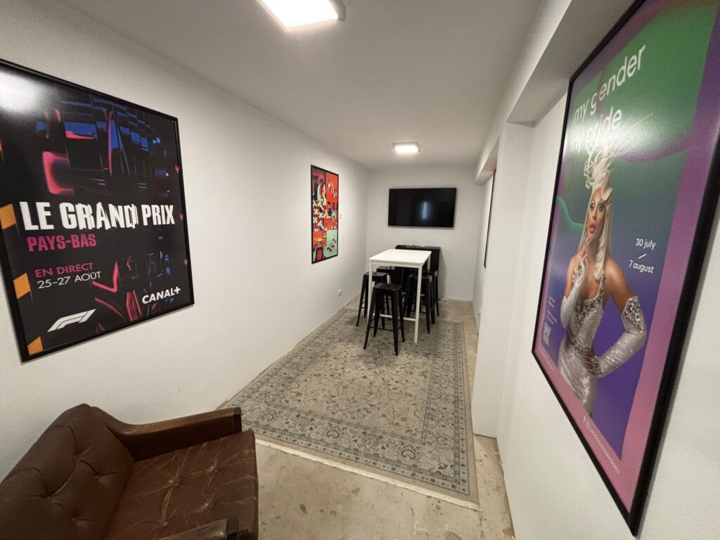 Een moderne zithoek aan de Van Ostadestraat met posters aan de muur, een hoge tafel met krukken en een televisie aan de wand.