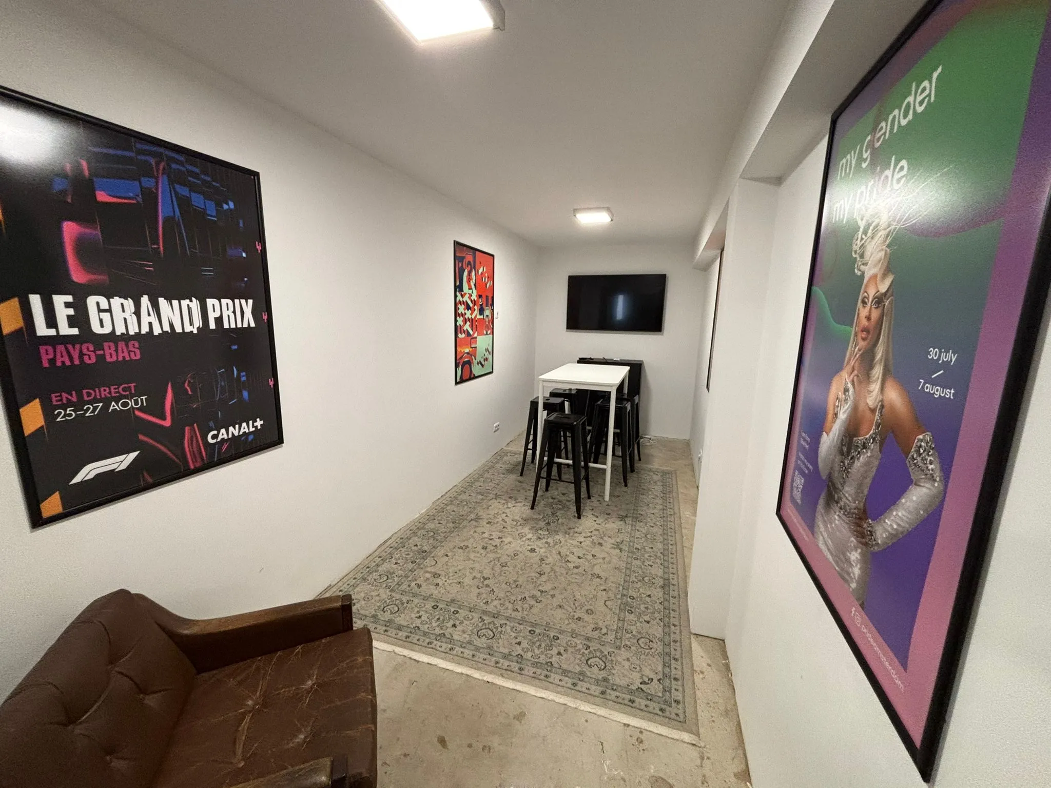 Een moderne zithoek aan de Van Ostadestraat met posters aan de muur, een hoge tafel met krukken en een televisie aan de wand.