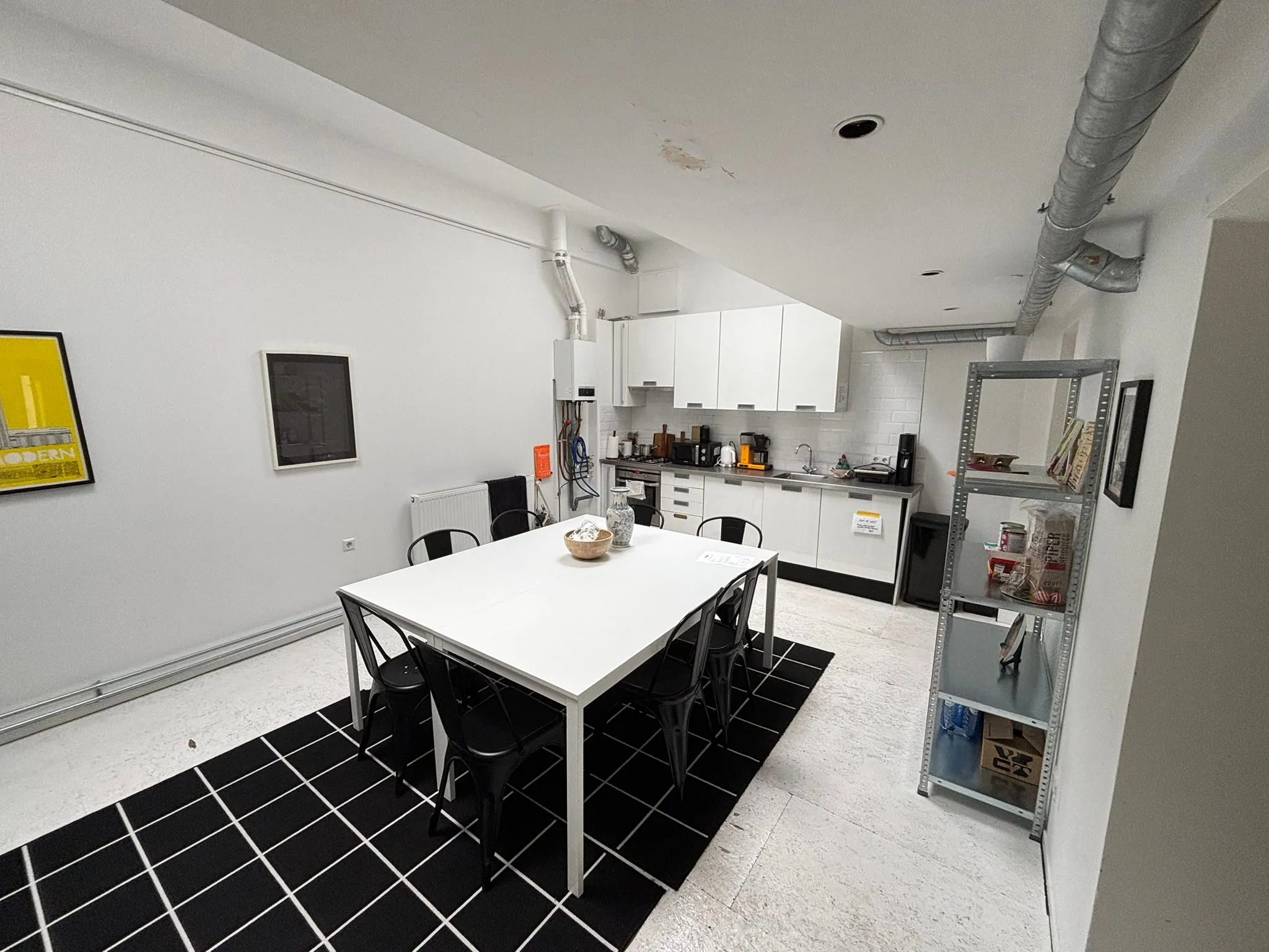 Moderne, witte keuken met een eettafel, zes zwarte stoelen en een open metalen rek, gelegen aan de Van Ostadestraat.