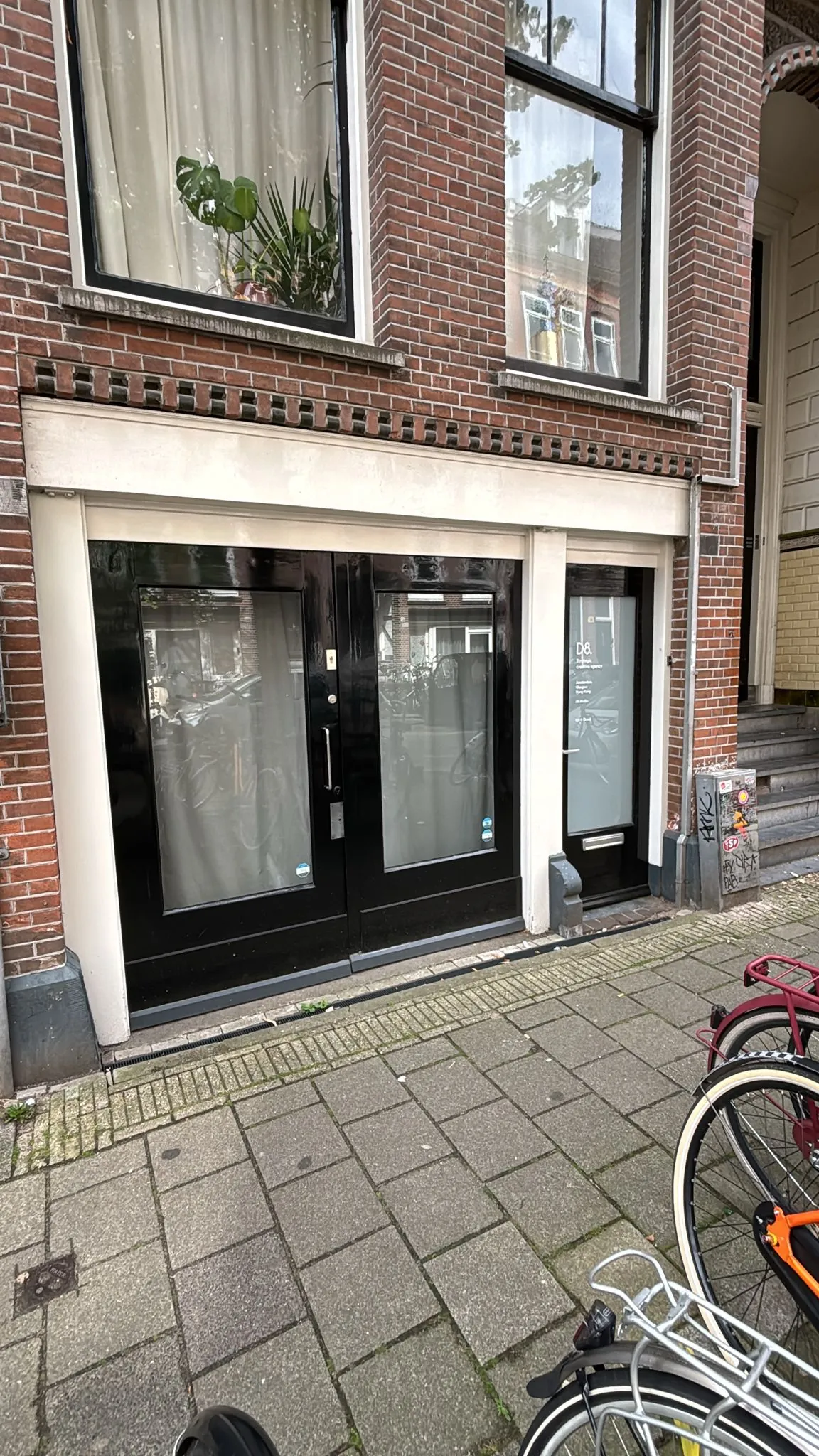 Ingang van een pand aan de Van Ostadestraat met zwarte deuren, ramen met gordijnen en geparkeerde fietsen op de stoep.