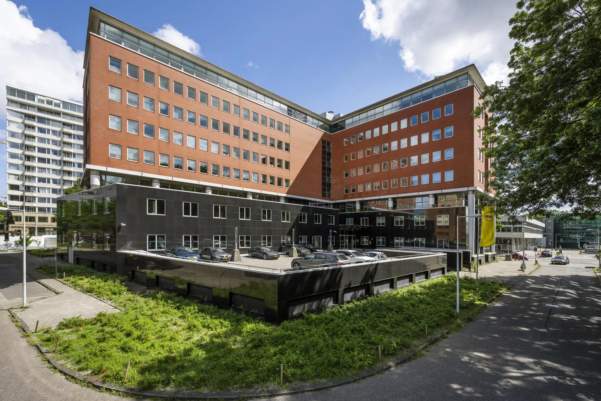 Kantoorgebouw aan het Koningin Wilhelminaplein in Amsterdam met een rode en zwarte gevel en een parkeerdek op de voorgrond.