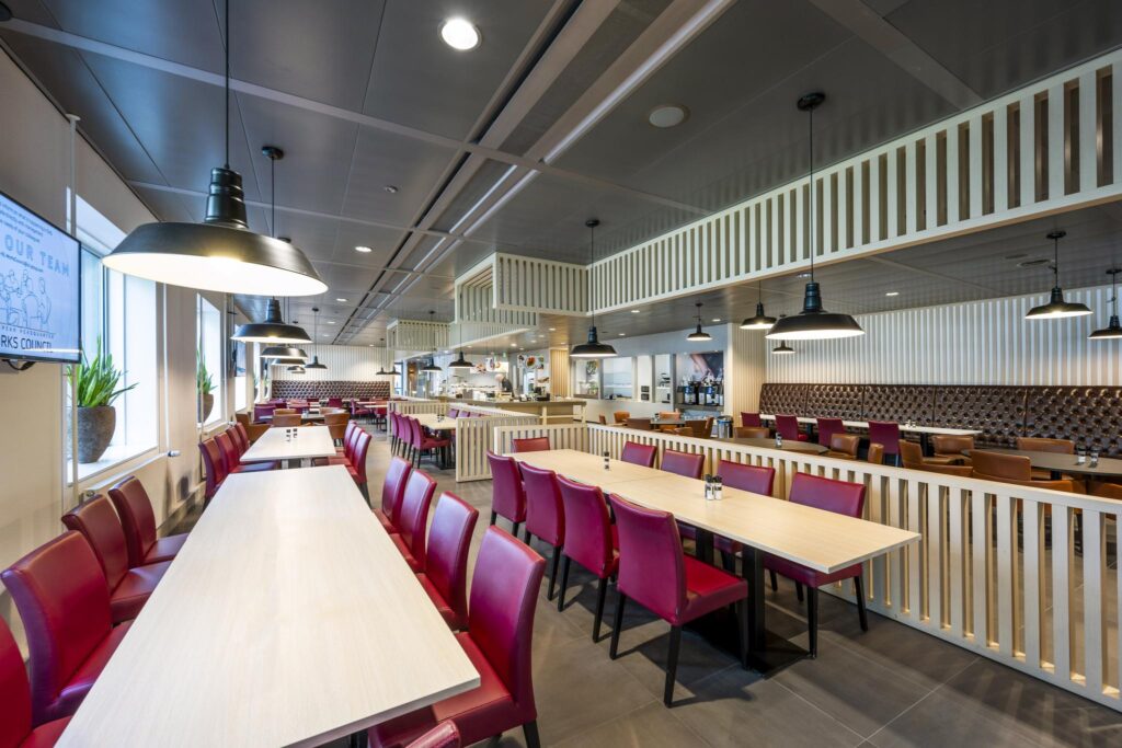 Moderne, licht ingerichte bedrijfskantine aan het Koningin Wilhelminaplein met houten tafels en rode stoelen.