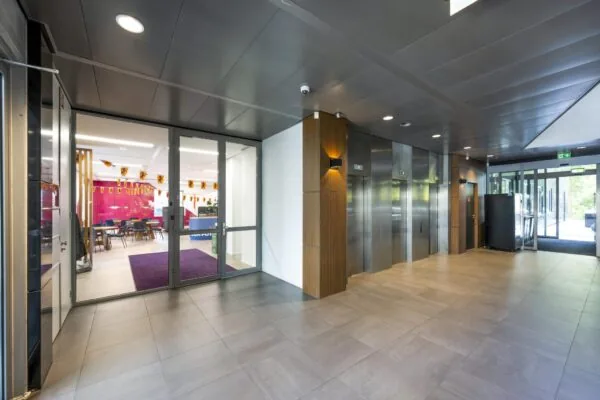 Moderne entreehal met liften en glazen deuren naar een kleurrijk ingericht kantoor aan het Koningin Wilhelminaplein.