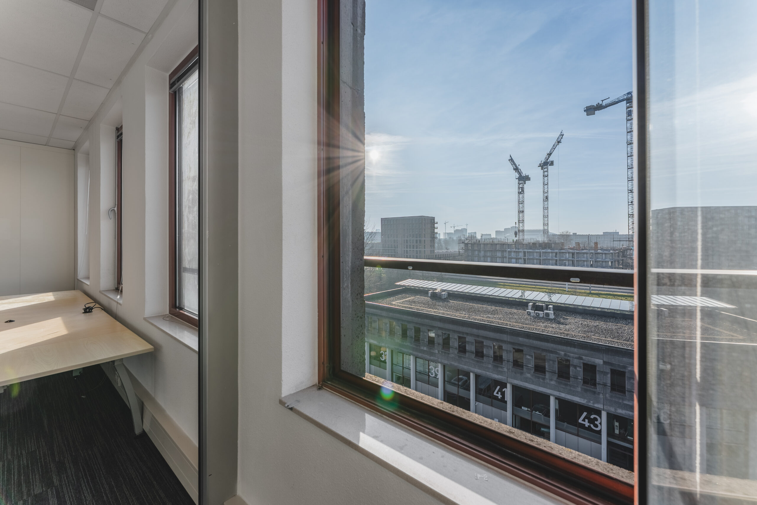 Uitzicht vanuit een kantoorraam op bouwkranen en een gebouw met nummers 41 en 43.