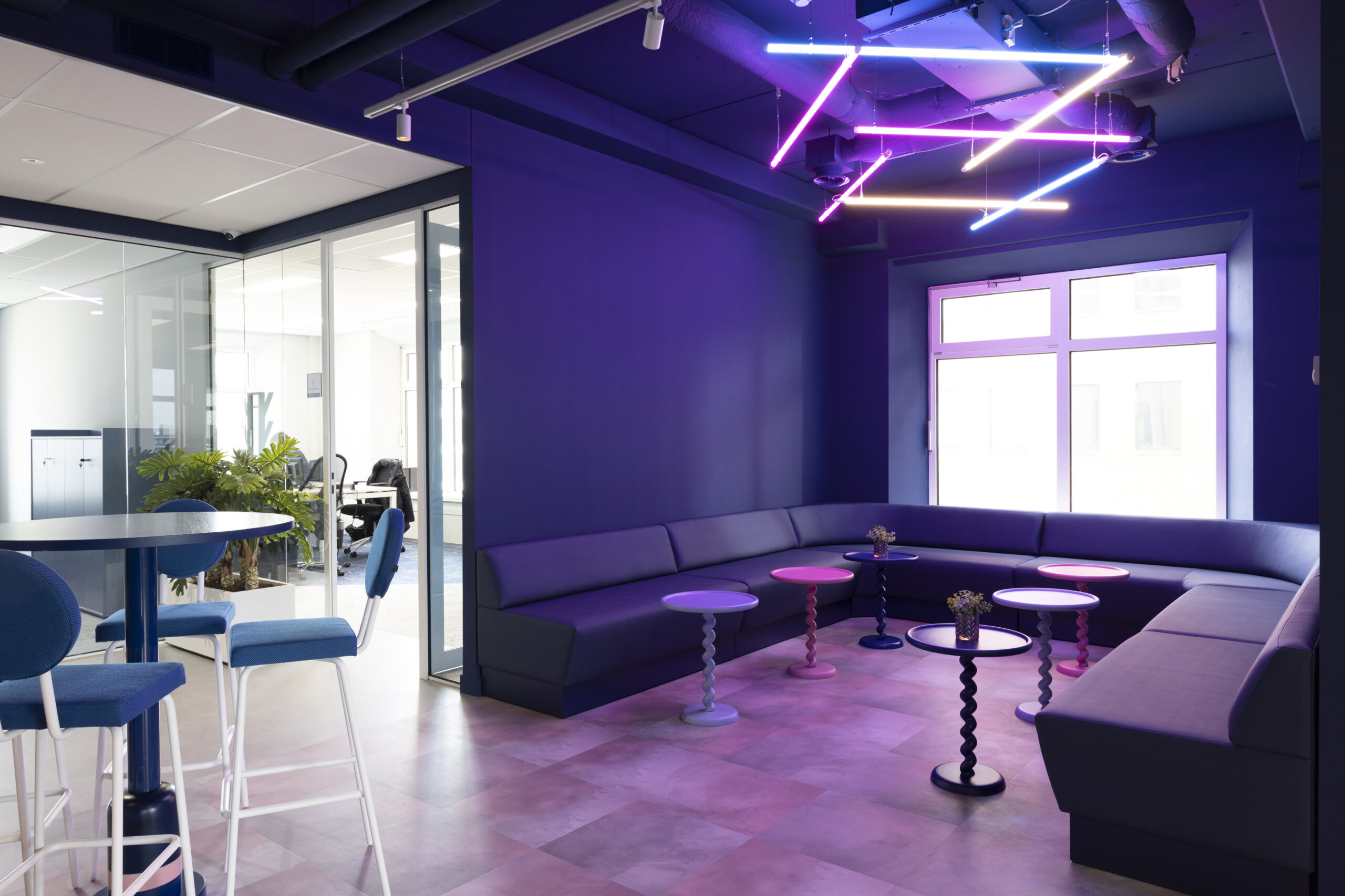 Moderne lounge met paarse neonverlichting, comfortabele zitbanken en bijzettafels in een kantoorruimte in Rotterdam.