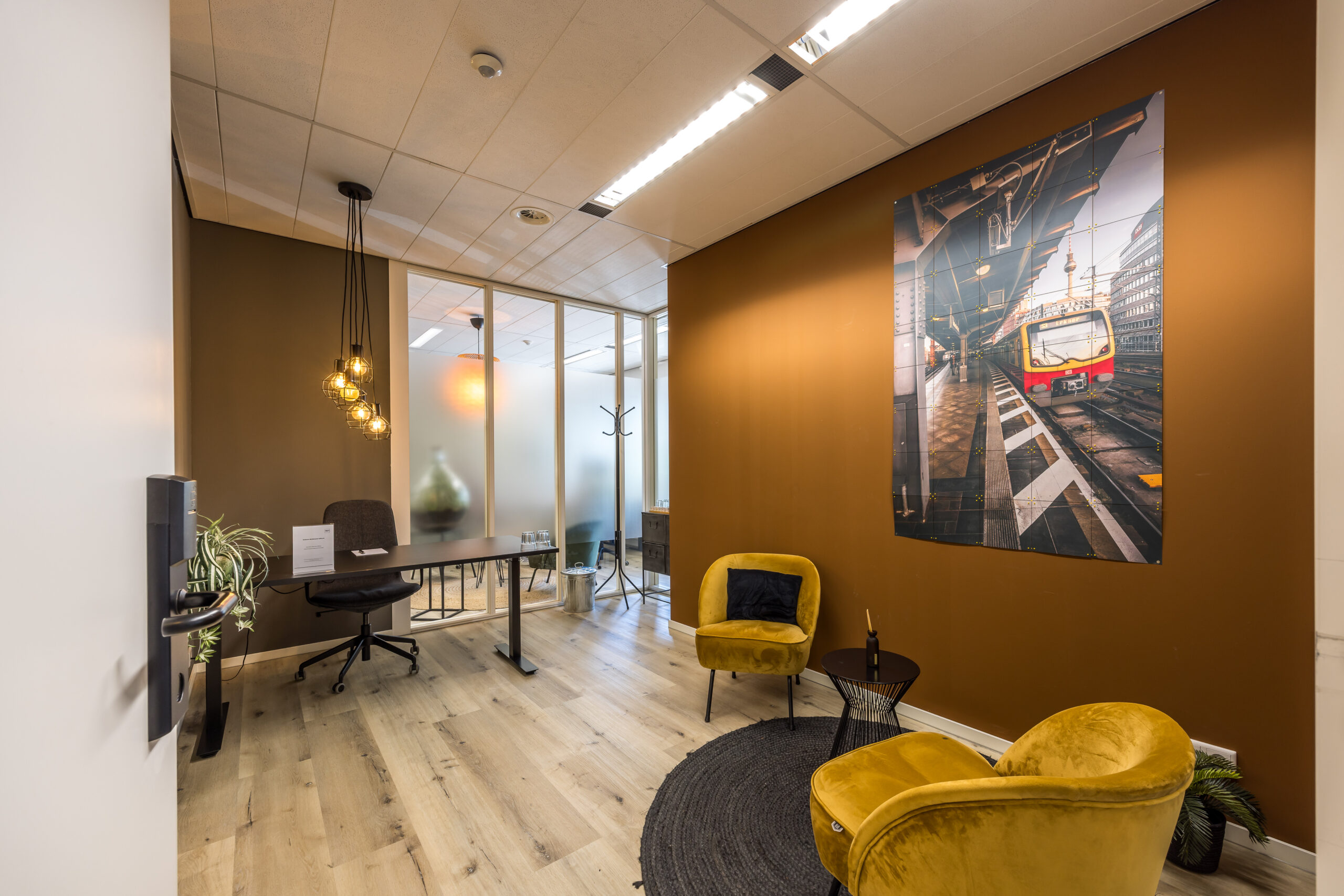 Moderne kantoorruimte met bruine muren, gele stoelen en een grote fotoposter van een trein op het station.