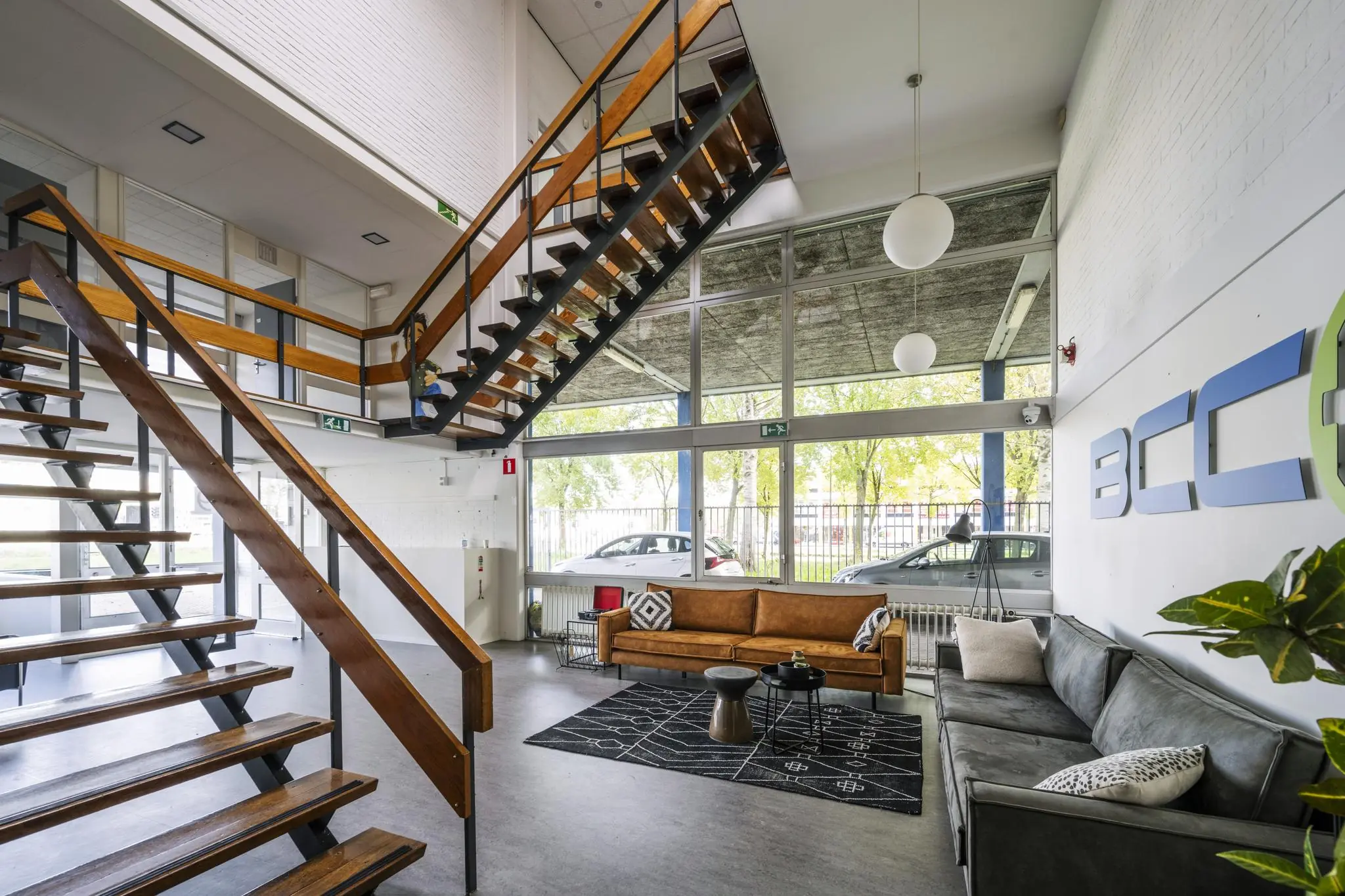 Moderne wachtruimte bij Van der Madeweg met zithoeken, open trap en groot raam met uitzicht op geparkeerde auto’s.