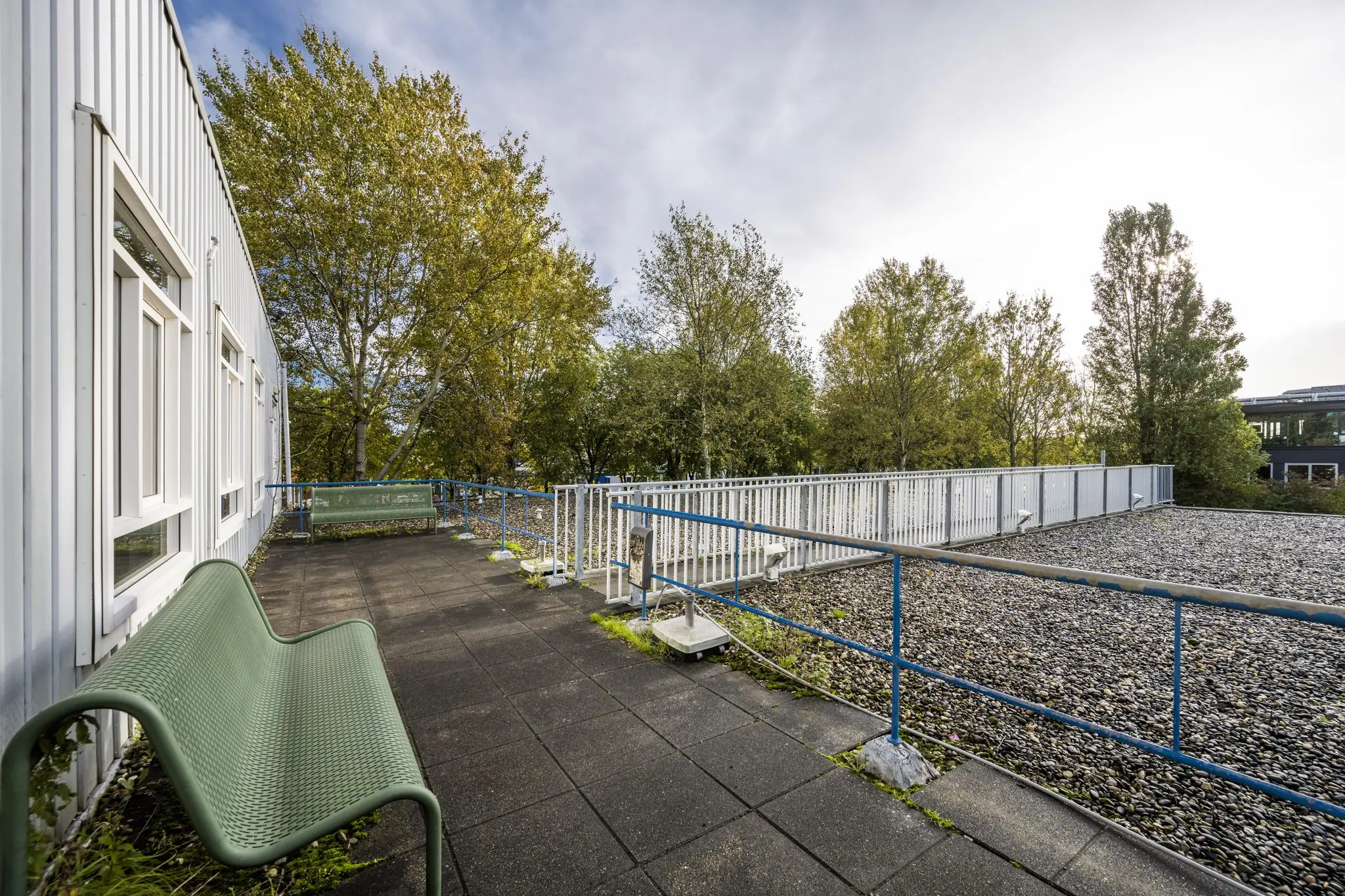 Dakterras met bankjes en uitzicht op bomen bij een gebouw aan de Van der Madeweg.
