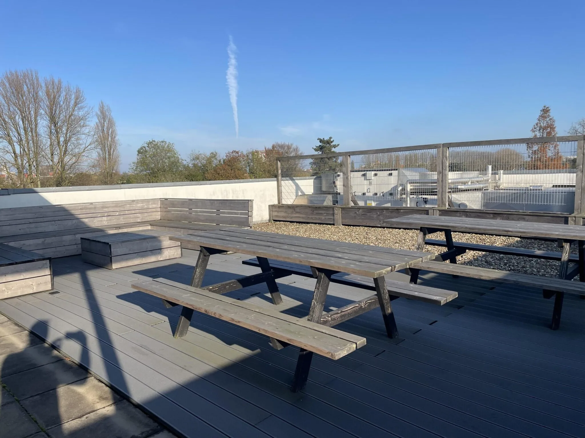 Dakterras aan de Jan Leentvaarlaan met houten picknicktafels en bankjes onder een blauwe lucht.