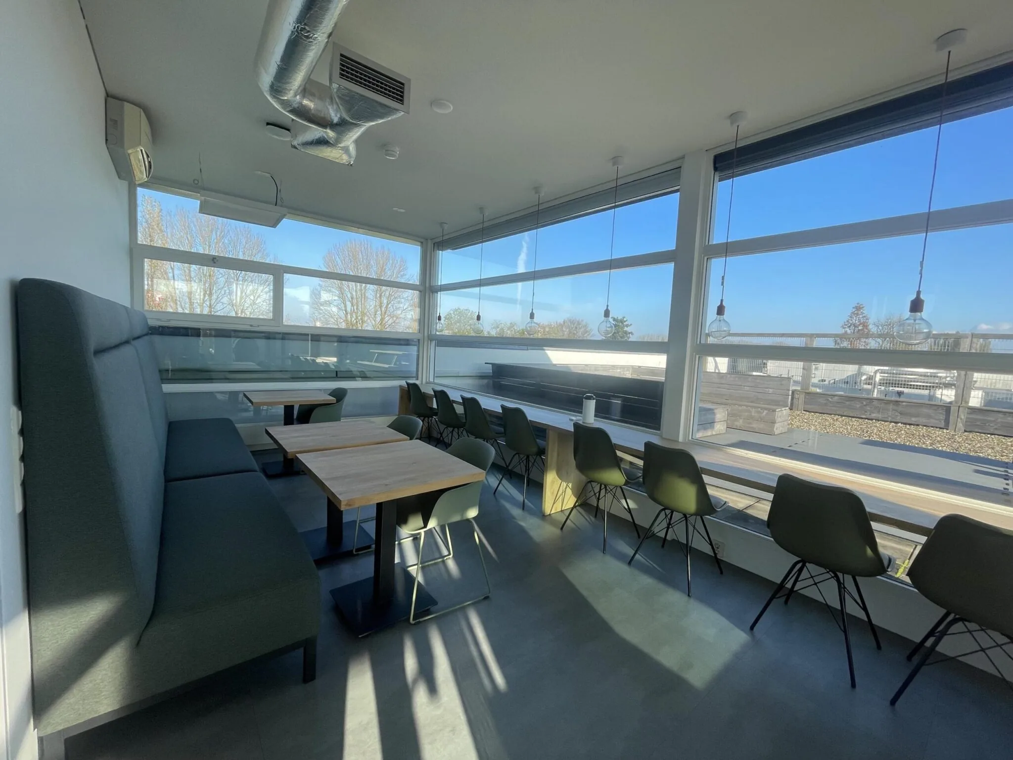 Modern ingerichte kantineruimte aan de Jan Leentvaarlaan met grote ramen en uitzicht naar buiten.