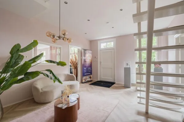 Moderne en sfeervolle ontvangstruimte van EMS Body Contour Studio aan de Sloterweg, met lichtroze muren, stijlvolle meubels en een witte spiltrap.