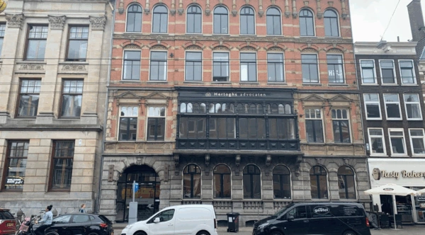 Voorgevel van het pand aan de Raadhuisstraat met het kantoor van Hertoghs advocaten en omliggende winkels en geparkeerde voertuigen.