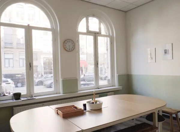 Een lichte vergaderruimte aan de Raadhuisstraat met grote boogramen, een houten tafel en uitzicht op de straat.