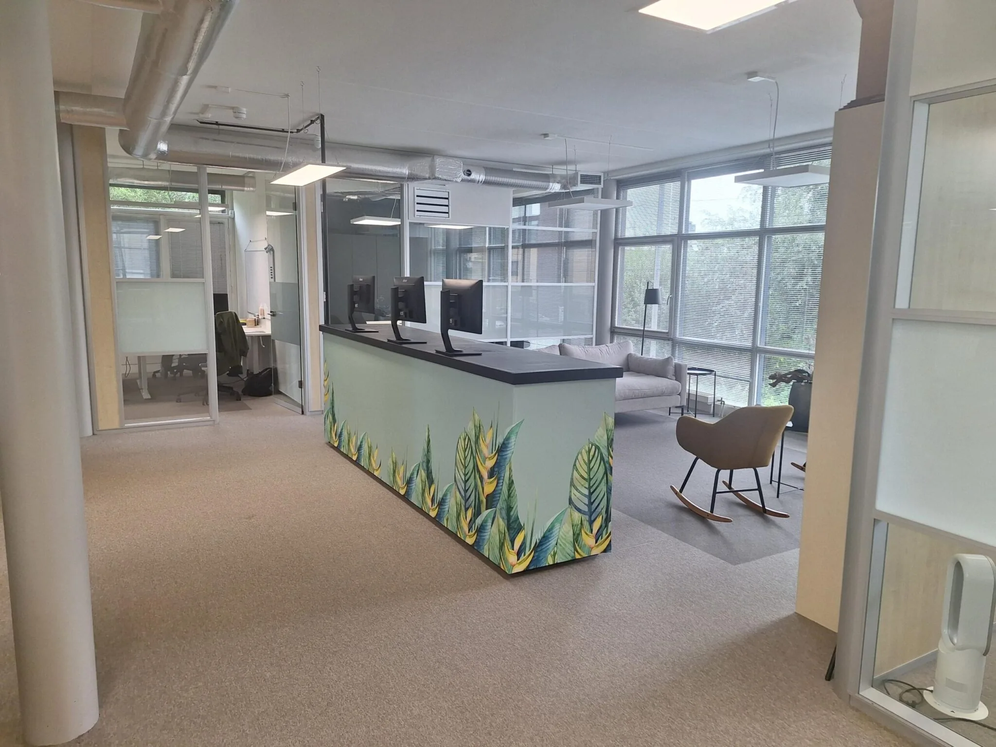 Modern kantoorinterieur aan de Jan Leentvaarlaan met een kleurrijke balie, werkplekken en zithoek bij grote ramen.