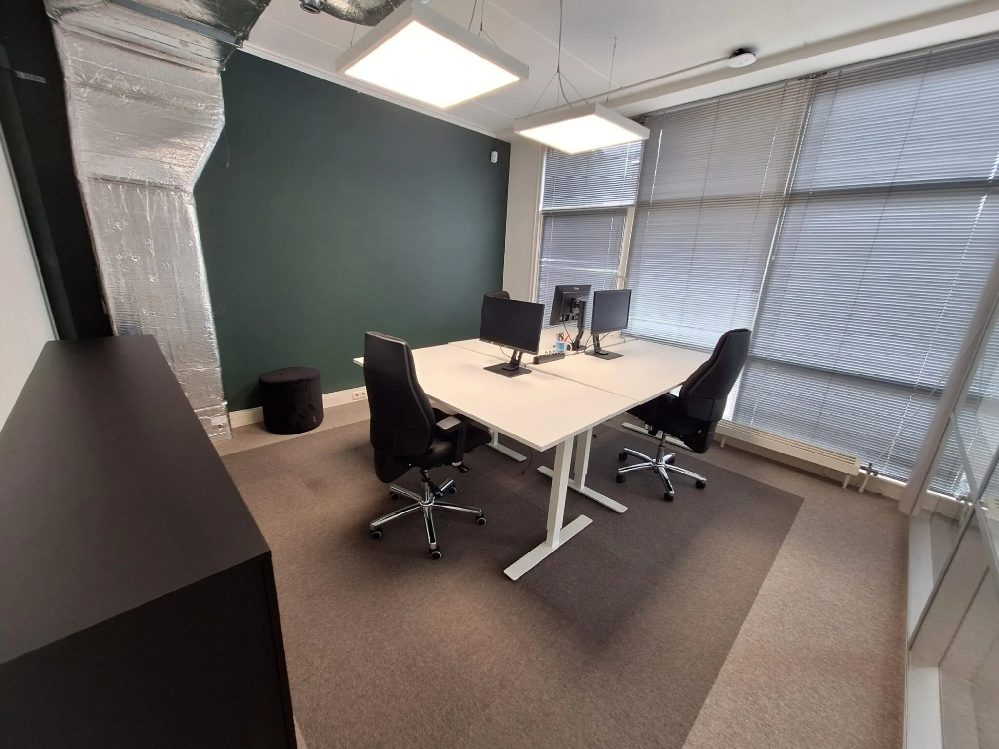 Modern ingericht kantoor met twee werkplekken aan de Jan Leentvaarlaan, voorzien van bureaustoelen, computers en grote raampartijen met jaloezieën.