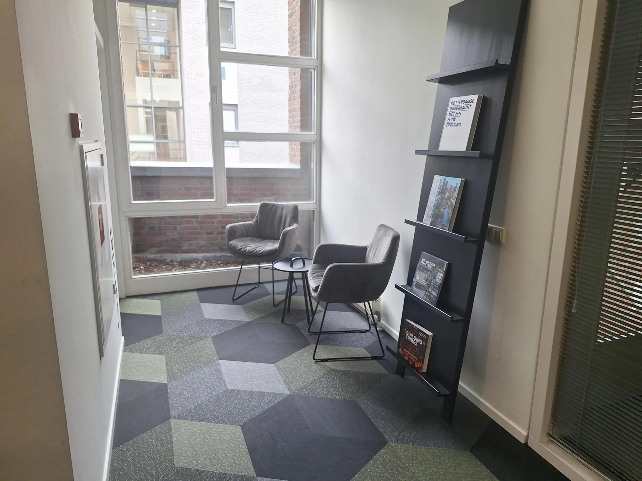 Zithoek met twee grijze stoelen, een tafeltje en een boekenkast in een wachtruimte aan de Jan Leentvaarlaan.