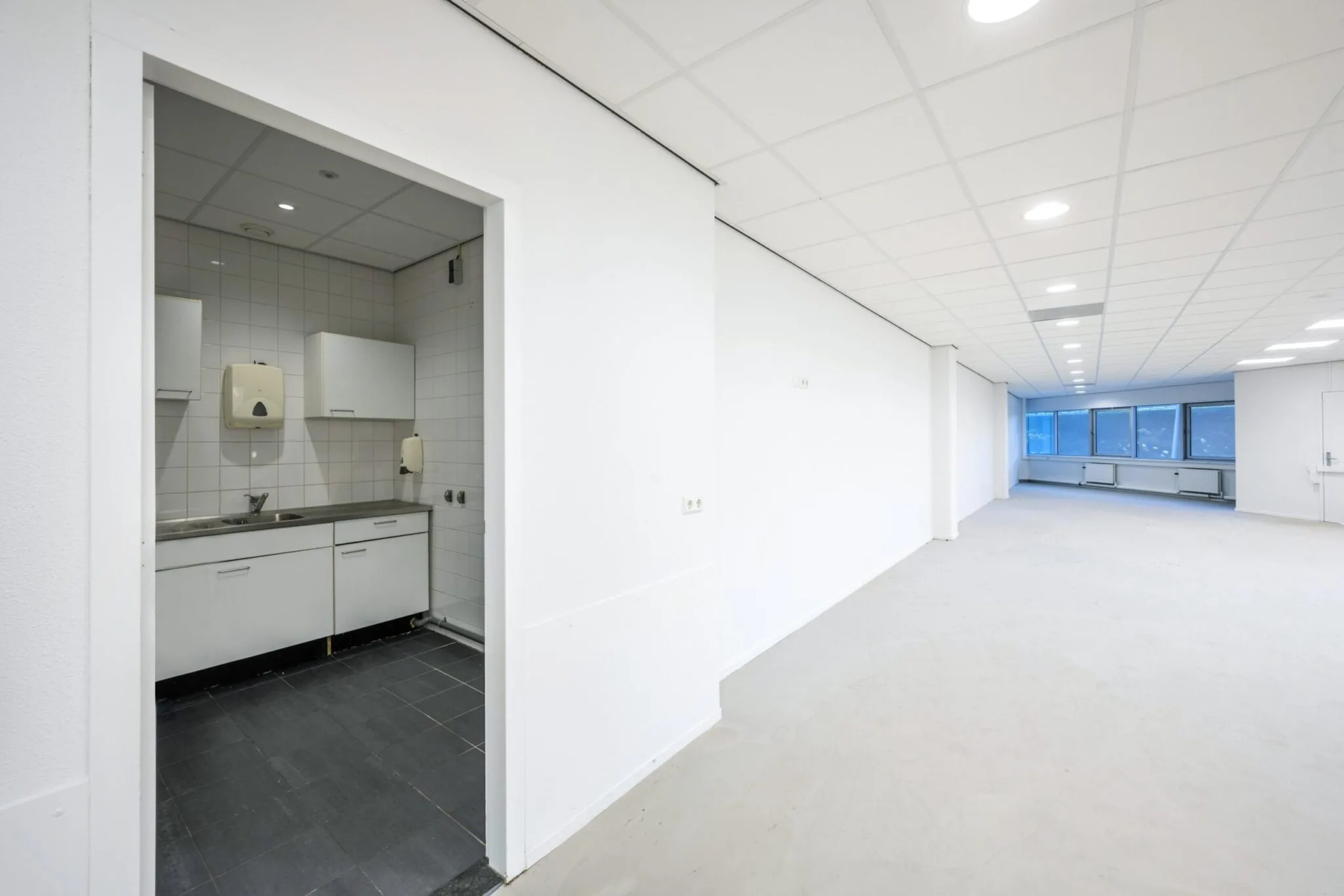 Lichte, lege kantoorruimte aan de Kuiperbergweg met een kleine pantry met witte keukenkastjes en tegelvloer.