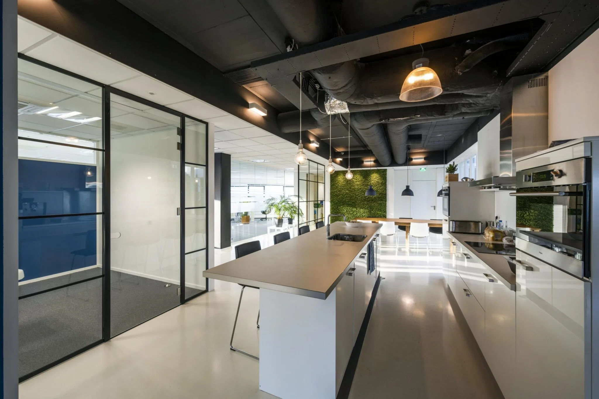 Moderne kantoorruimte aan de Kuiperbergweg met open keuken, glazen vergaderruimte en groene plantenwand.