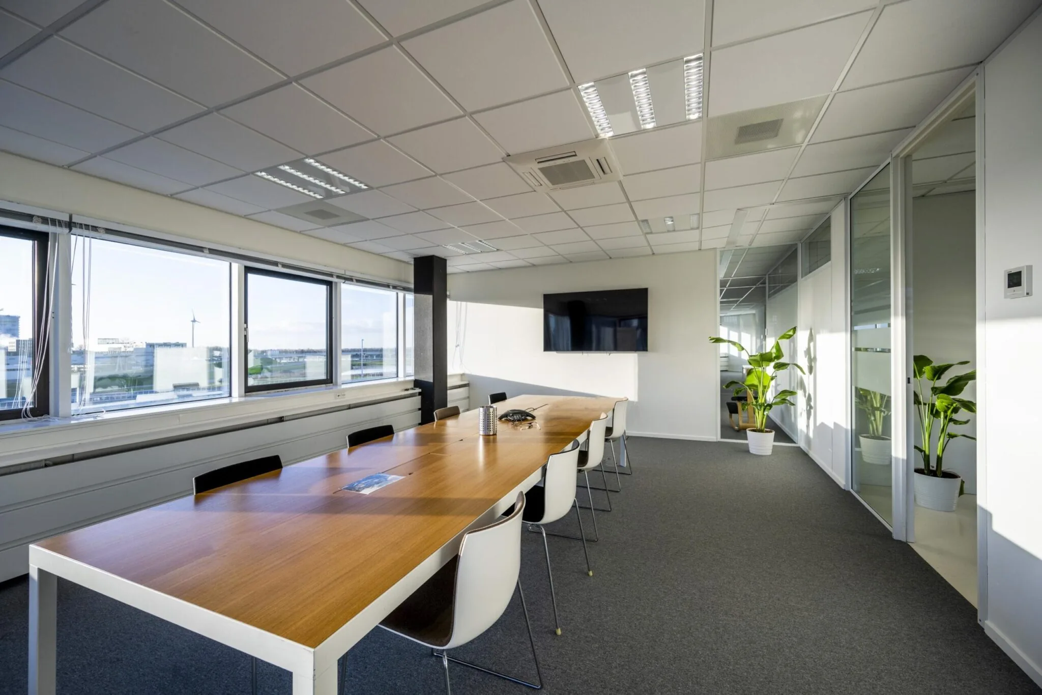 Vergaderruimte aan de Kuiperbergweg met lange houten tafel, witte stoelen, flatscreen en grote ramen met uitzicht.