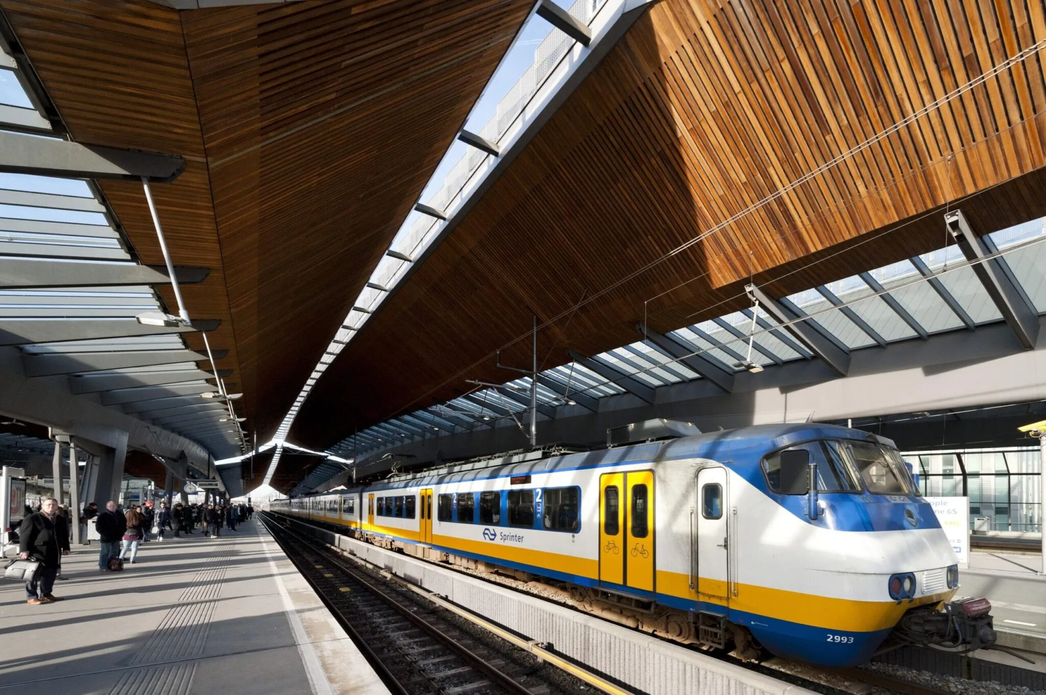 NS Sprinter-trein staat klaar op een perron onder het kenmerkende houten dak van station Arnhem Centraal.