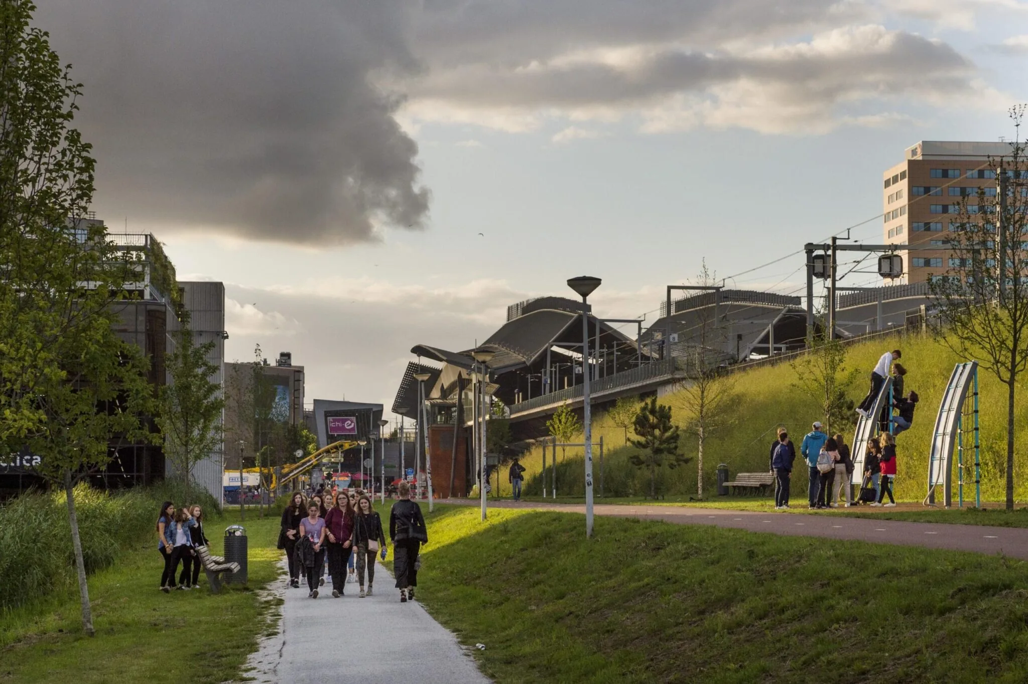 Groep mensen wandelt over de Kuiperbergweg in Amsterdam-Zuidoost langs een park en station.
