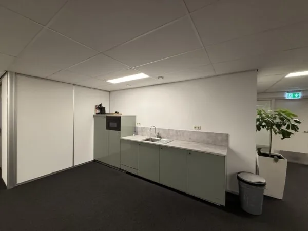 Kleine kantoorpantry met gootsteen, ingebouwde magnetron en een plant in de hoek bij Vlierberg 175.