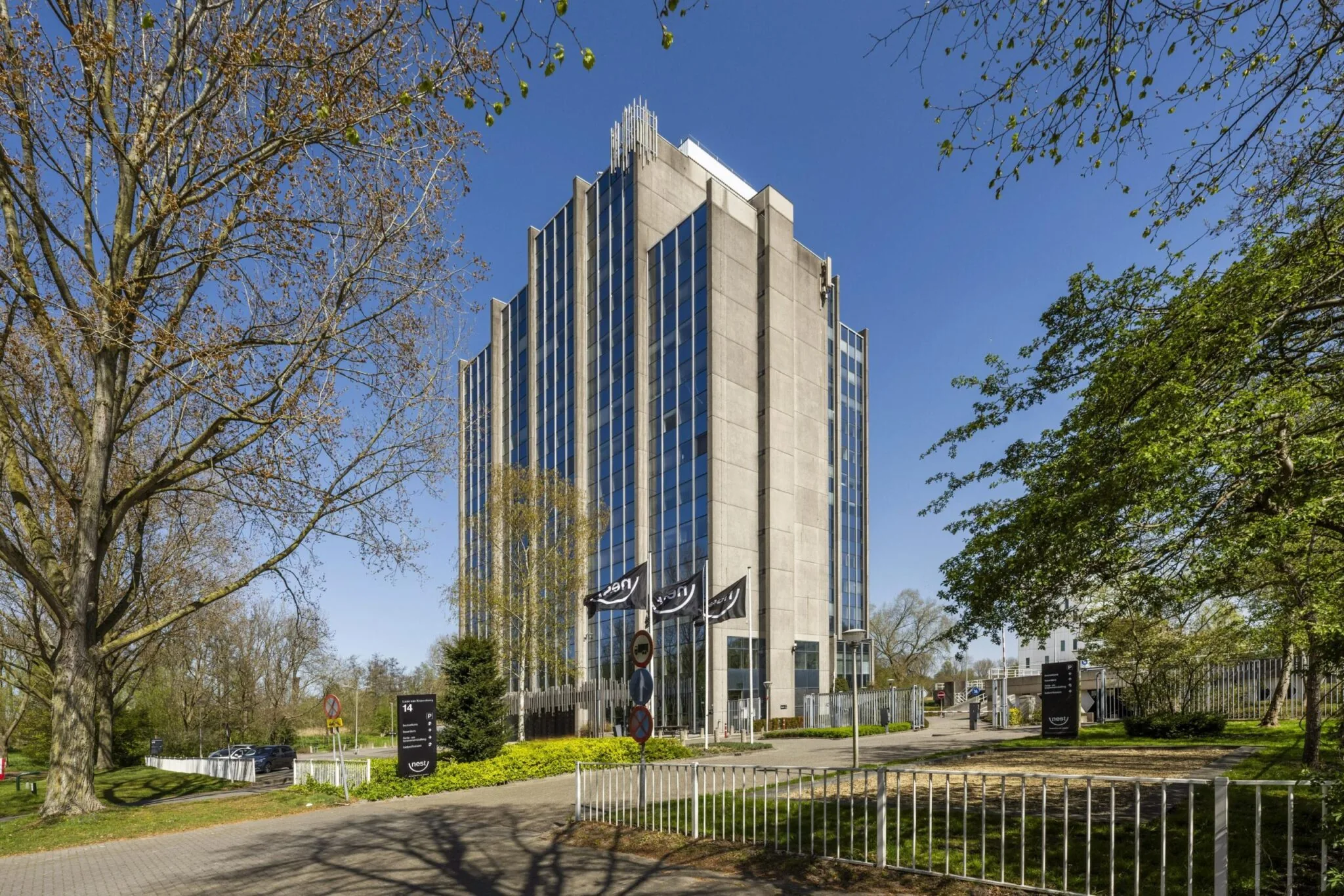 Modern kantoorgebouw aan de Laan van Kronenburg omgeven door bomen en een blauwe lucht.