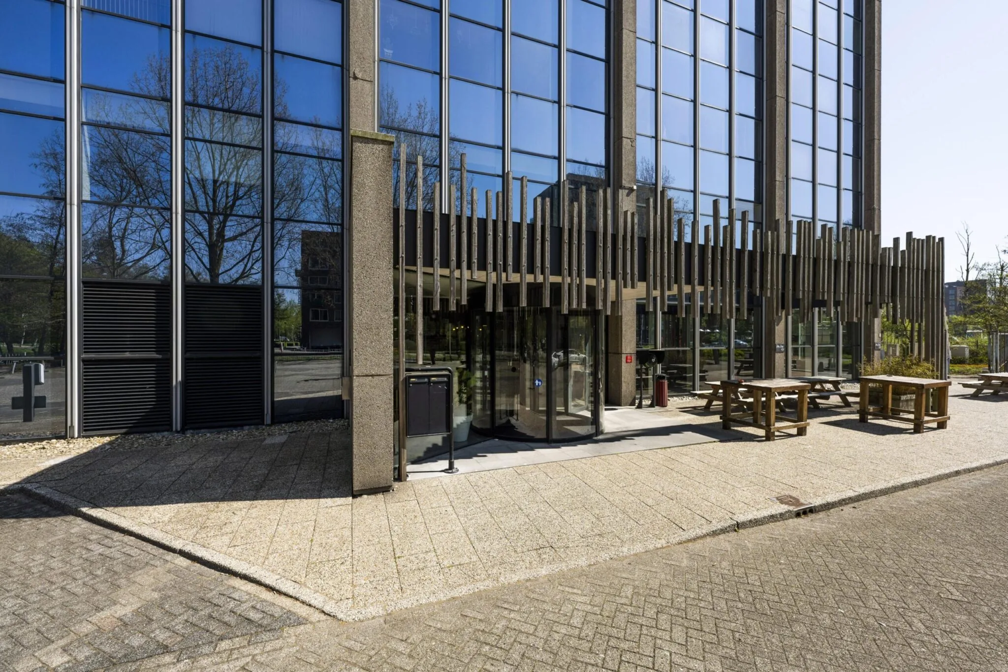 Ingang van een modern kantoorgebouw aan de Laan van Kronenburg met glazen gevel en zitbanken buiten.