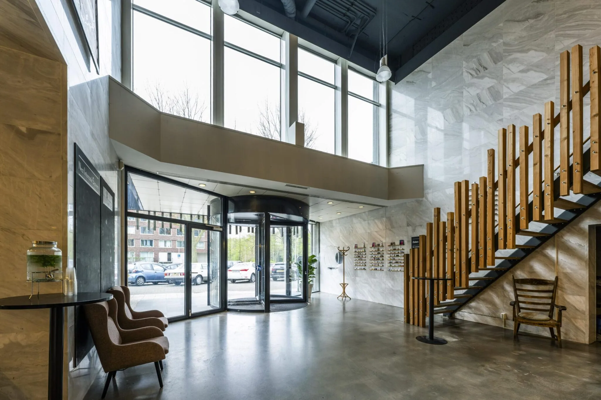 Moderne ontvangsthal van een kantoorpand aan de Laan van Kronenburg met glazen draaideur, houten trap en veel daglicht.