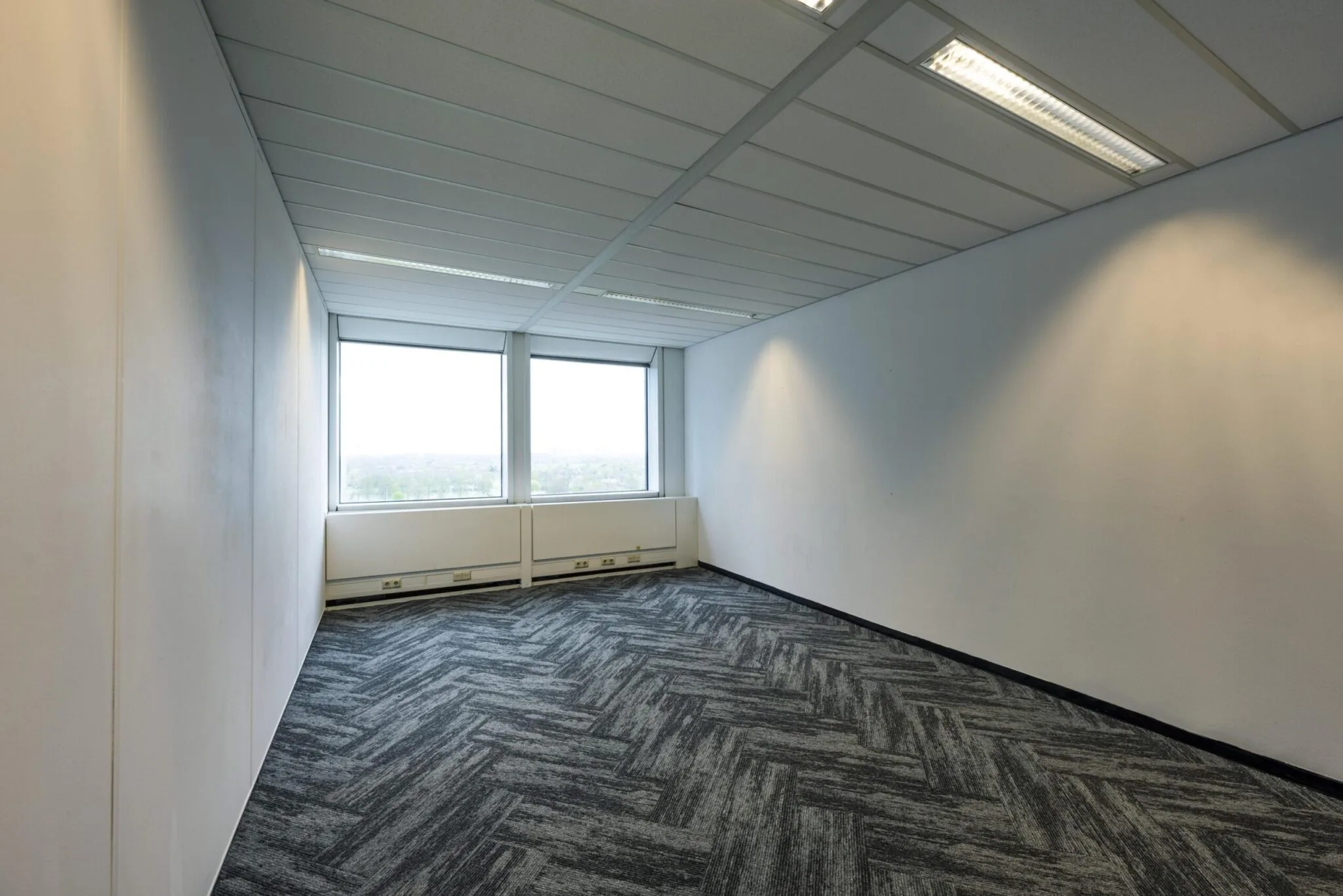 Lege kantoorruimte aan de Laan van Kronenburg met twee grote ramen en tapijtvloer in visgraatpatroon.
